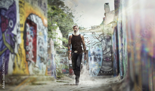 Porträt eines bärtigen Bikers, der in der Stadt vor Graffiti bemalten Wand läuft © Cara-Foto