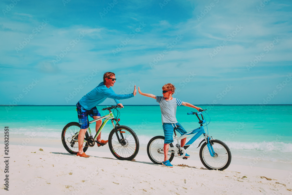 happy father and son biking on beach