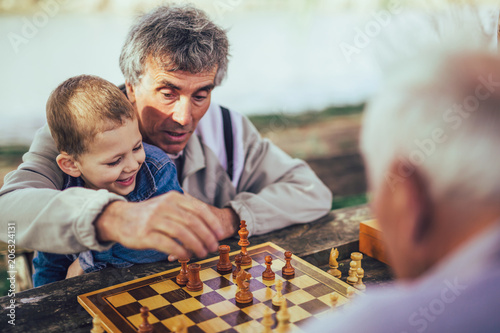Active retired people, old friends and free time, two senior men having fun and playing chess at park, spend time with grandson