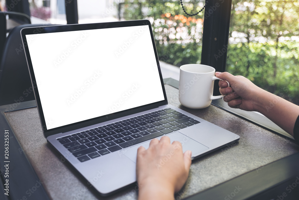 Mockup image of a woman using laptop with blank white desktop screen while drinking hot coffee in cafe Mockup image of a woman using laptop with blank white desktop screen while drinking hot coffee in cafe