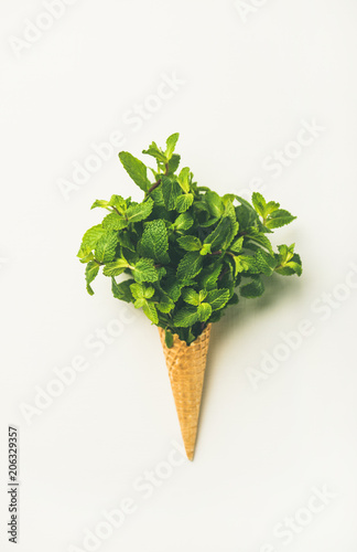 Flat-lay of waffle sweet cone with fresh leaves mint over white background, top view. Spring or summer mood concept
