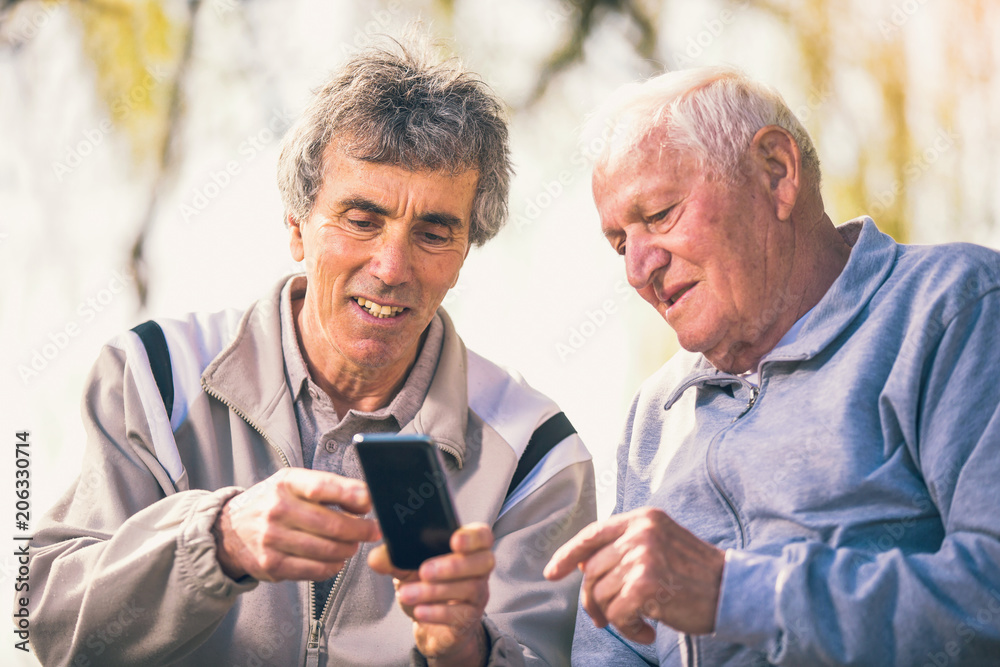 Two senior men using smart phone in the park Two senior men using smart phone in the park