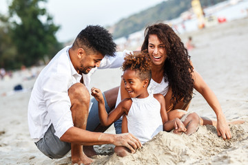 Young mixed race family sitting and relaxing at the beach on beautiful summer day.Playing in the sand.