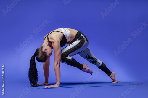 Long haired beautiful pilates or yoga athlete does a graceful pose while wearing a tight sports outfit against a bright blue background in a studio