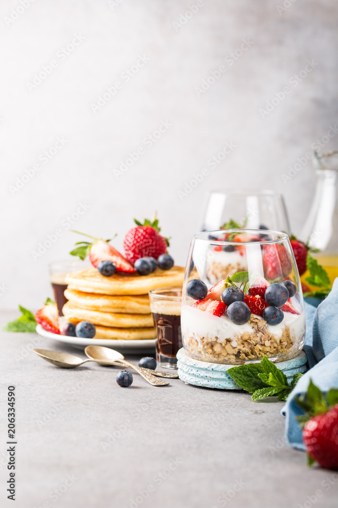 Healthy breakfast with oatmeal granola with berries and yogurt and panccakes on light gray concrete background. Healthy food concept with copy space. Healthy breakfast with oatmeal granola with berries and yogurt and panccakes on light gray concrete background. Healthy food concept with copy space.