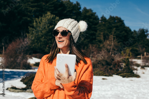 Young and cheerful woman using her tablet, to stay connected with her family, on the mountain a day of snow and sun. Lifestyle.