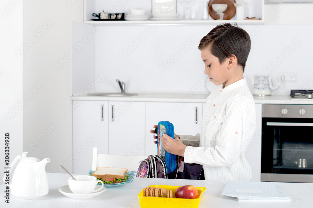 A schoolboy gathers a backpack to school. He puts a pencil case and a box of lunch in a school bag, A schoolboy gathers a backpack to school. He puts a pencil case and a box of lunch in a school bag,