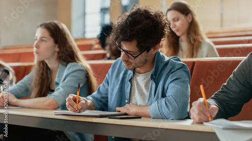 Hispanic Young Man Among His Fellow Students in the Classroom. Young Bright People Listening to a Lecture and Take Notes while Studying at the University.