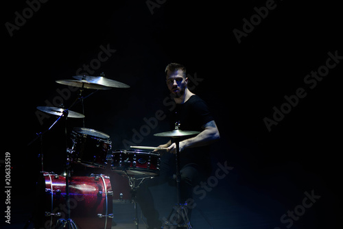 music, people, musical instruments and entertainment concept - male musician with drumsticks playing drums on the stage.