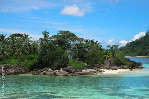 Beautiful view of one of the islands of Seychelles in the Indian Ocean. On the island lie huge stones. Evergreen vegetation is in the foreground.