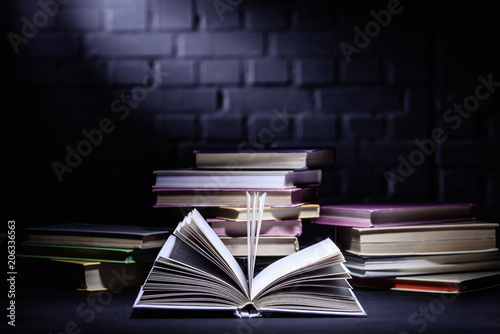 open book in front of stack of books on dark surface