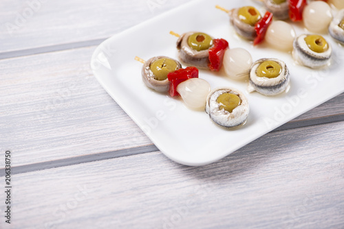 Banderillas of olives with spring onion and anchovies in a white plate on wooden table. Typical spanish food.