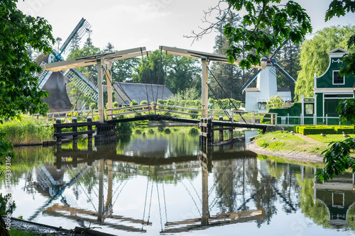 Water reflection of bridge, wind mills and a traditional dutch building at Arnhem Open - air and national heritage museum, in Arnhem, Netherlands