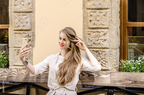 Portrait of a smiling bussines casual woman doing selfie on smartphone mobile cell with long hair in city street sunny day background