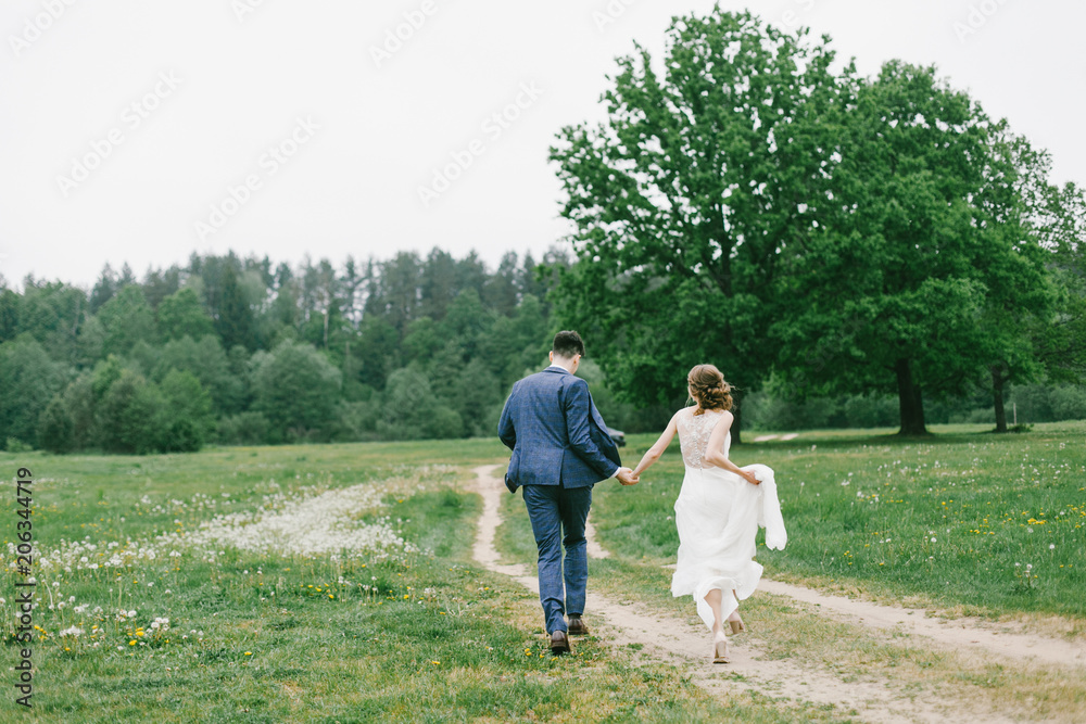 Stylish couple of newlyweds on their wedding day. Happy young bride, elegant groom running away holding hands