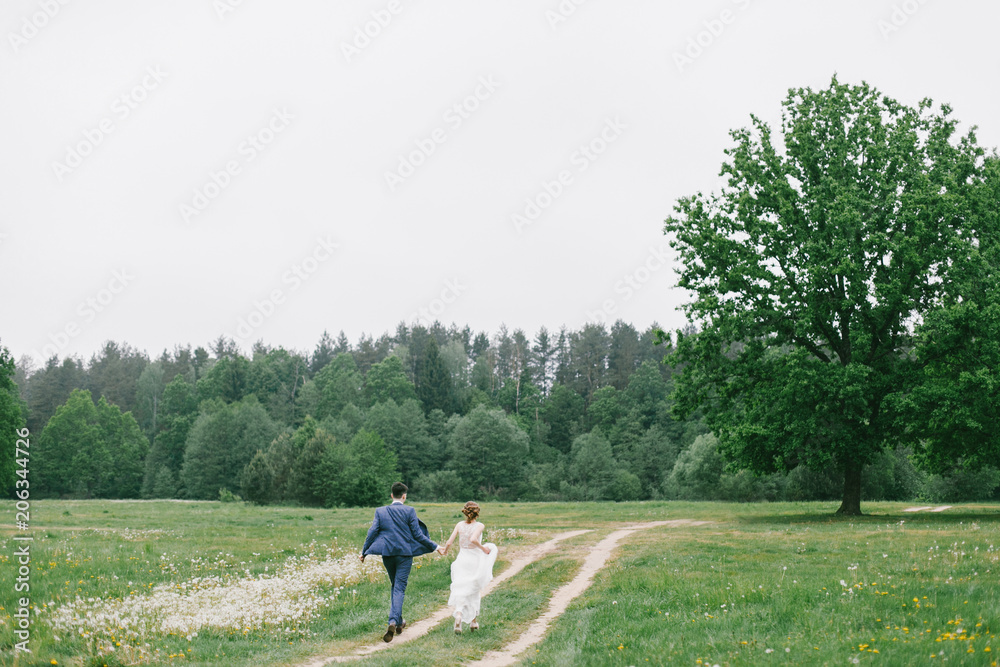 Stylish couple of newlyweds on their wedding day. Happy young bride, elegant groom running away holding hands Stylish couple of newlyweds on their wedding day. Happy young bride, elegant groom running away holding hands