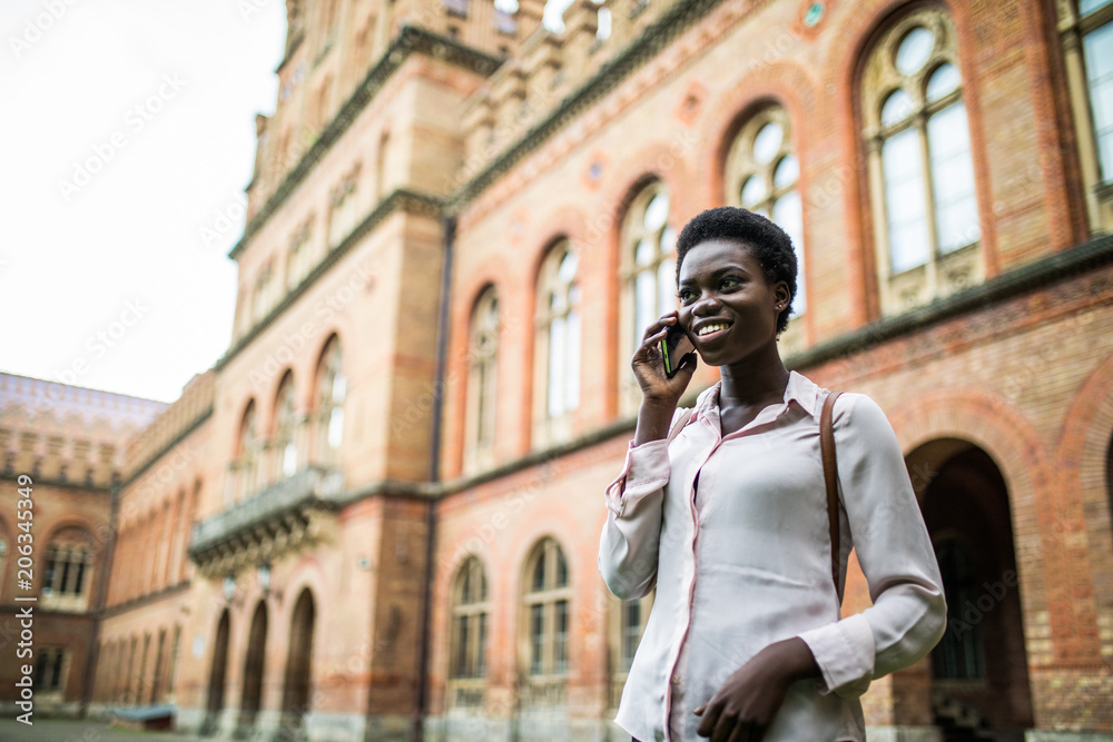 Portrait of pretty black woman in urban background talking on phone. Young student talking on phone at campus