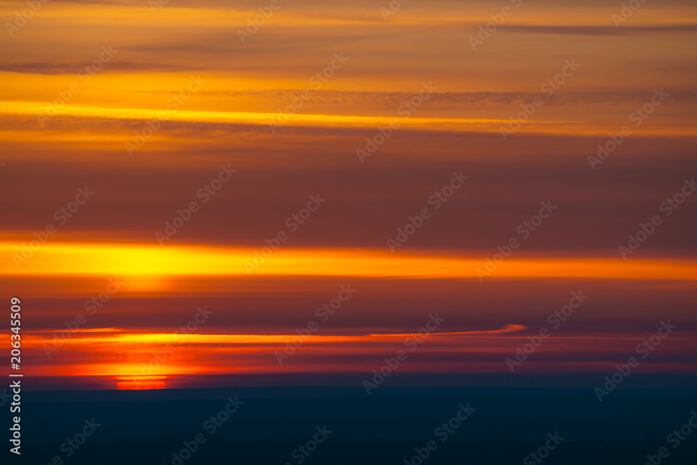 Big red sun circle rises out from behind dark horizon on background varicolored clouds of warmly shades. Beautiful background of dawn on picturesque cloud sky.