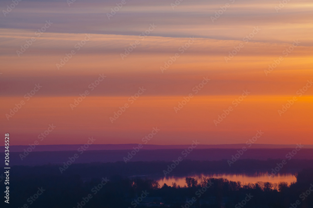 River under varicolored striped warm sky. Horizontal lines of picturesque clouds. Atmospheric background image of lake with reflection of dawn sky.