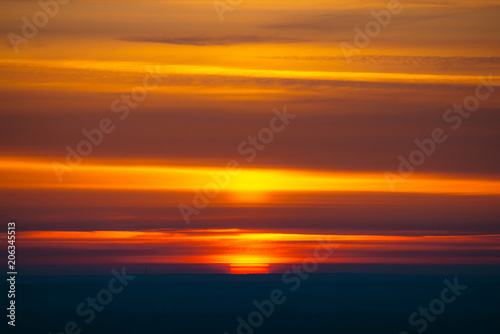Big red sun circle rises out from behind dark horizon on background varicolored clouds of warmly shades. Beautiful background of dawn on picturesque cloud sky. Sun in center.