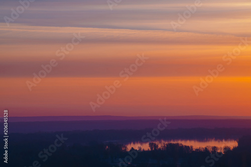 River under varicolored striped warm sky. Horizontal lines of picturesque clouds. Atmospheric background image of lake with reflection of dawn sky.