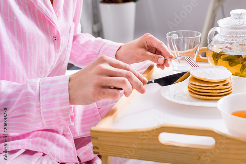 partial view of woman in pajamas having pancakes for breakfast in bed at home