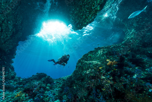 woman diver underwater at the entrance of a cave with sunrays photo