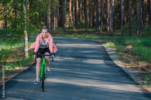 Girl on a bicycle in a pink hoodie in the park. Races on a bicycle. Active way of life and playing sports.