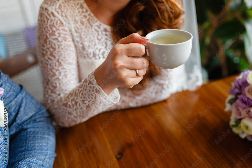 Young couple in a cafe in the attic drinking coffee and tea, sitting. Morning breakfast at the hotel. Cropped image of couple in love holding hands on wooden table while drinking coffee. Young couple in a cafe in the attic drinking coffee and tea, sitting. Morning breakfast at the hotel. Cropped image of couple in love holding hands on wooden table while drinking coffee.