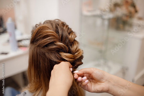 Close-up of woman hairdresser weaving plaits in beauty salon.