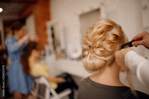 Hairdresser woman conducts training for pupil in salon, weaving braid hair, wedding styling.