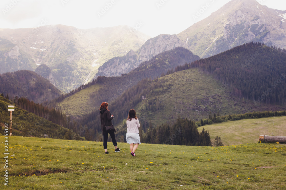 Two young girls walking on a green meadow among the mountains Two young girls walking on a green meadow among the mountains