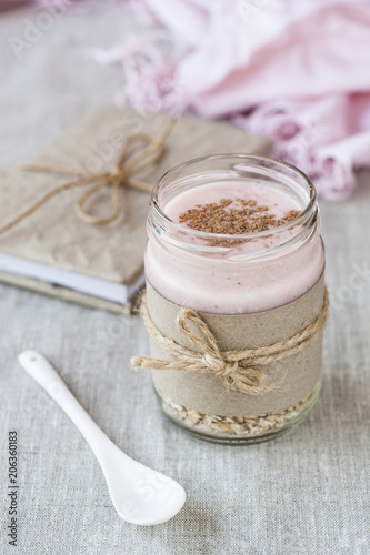 Oatmeal  flavored with yogurt  sprinkled with cinnamon in a glass jar. Next is a craft notebook and a pink napkin.