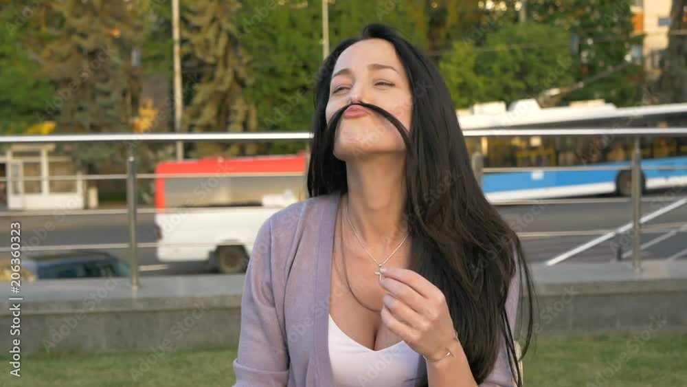 Young woman is playing with her hair portraying a mustache. Lovely girl having fun on the street. Chain with a cross on the neck. Young woman is playing with her hair portraying a mustache. Lovely girl having fun on the street. Chain with a cross on the neck.