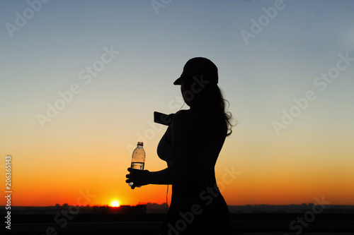 Silhouette of young woman with bottle of water on the sunset backgrounds. 