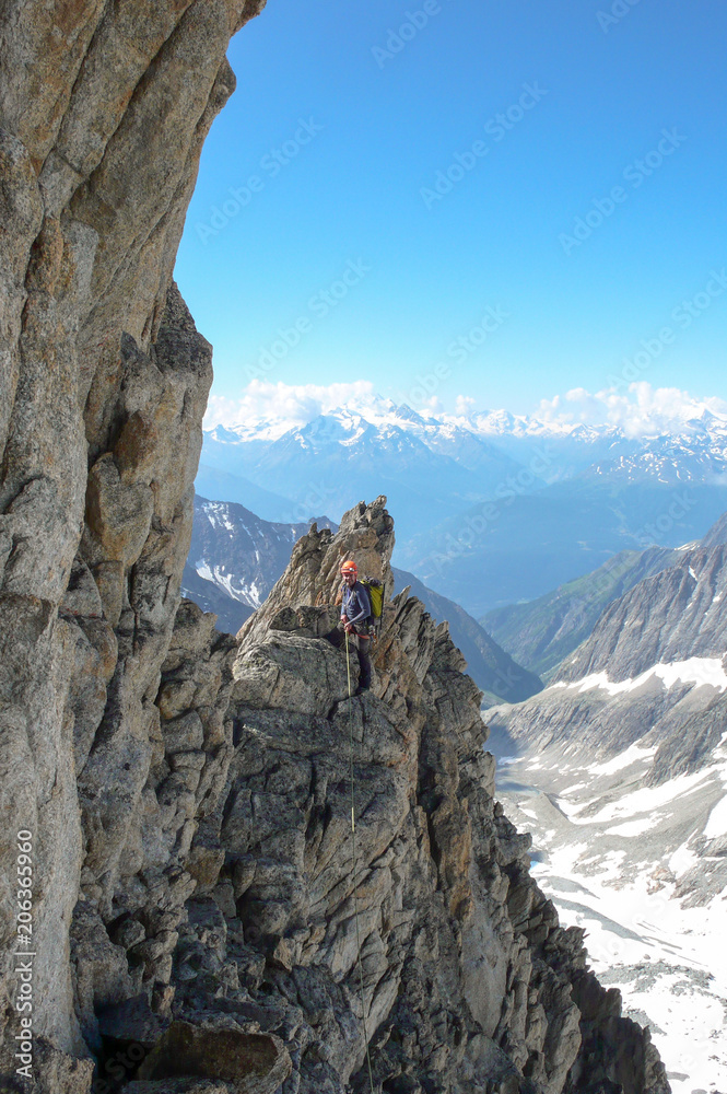male mountain guide lead climbing on an exposed granite ridge in the Alps