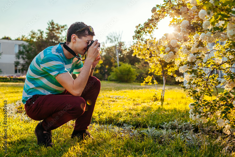Man photographer taking pictures of flowers in park at sunset. Young guy enjoys his hobby outside. Man photographer taking pictures of flowers in park at sunset. Young guy enjoys his hobby outside.