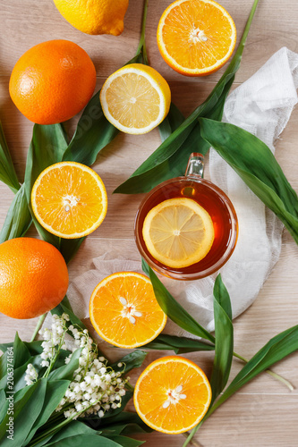 A cup of tea, sliced oranges, lemon and a bouquet of lilies of the valley on a wooden background. Healthy breakfast. The concept. Creative layout. Flat lay