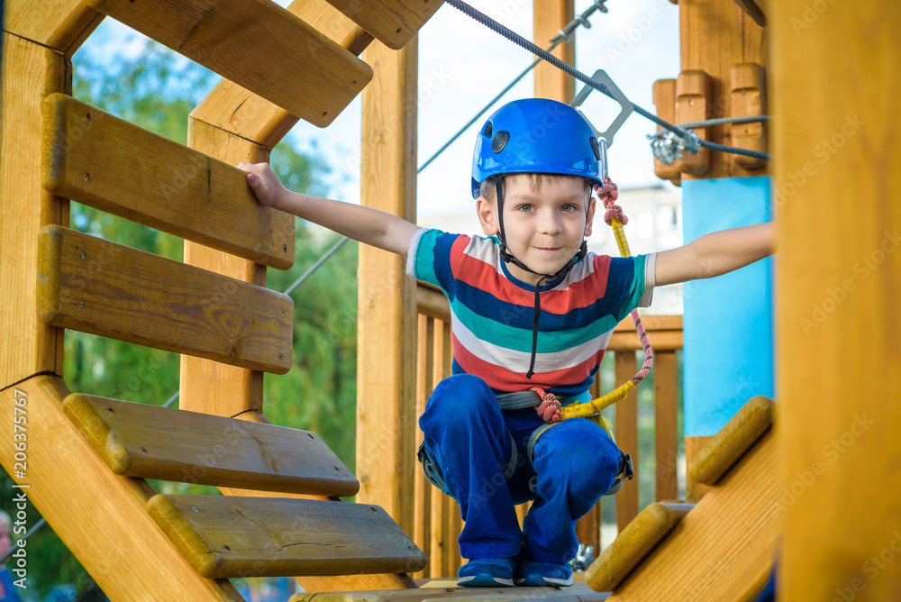 Happy boy having fun and playing at adventure park, holding ropes and climbing wooden stairs Happy boy having fun and playing at adventure park, holding ropes and climbing wooden stairs