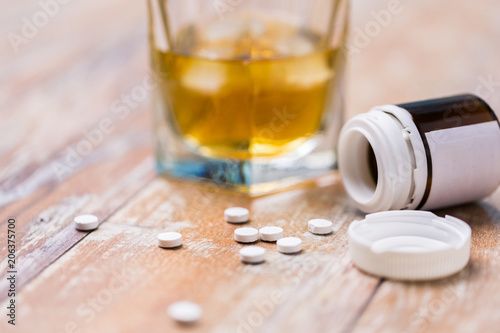 drug abuse, addiction and suicide concept - glass of alcohol and pills on table