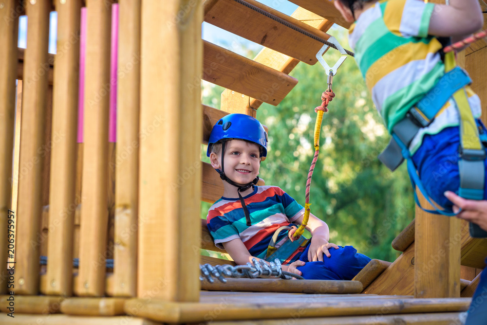 Little cute boy enjoying activity in a climbing adventure park on a summer sunny day. toddler climbing in a rope playground structure.