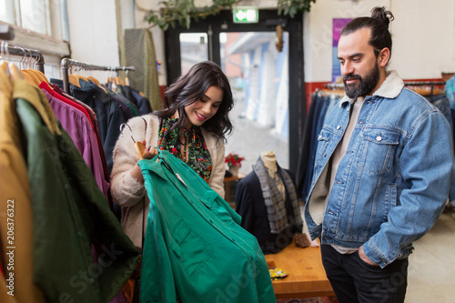 sale, shopping, fashion and people concept - happy couple choosing clothes at vintage clothing store