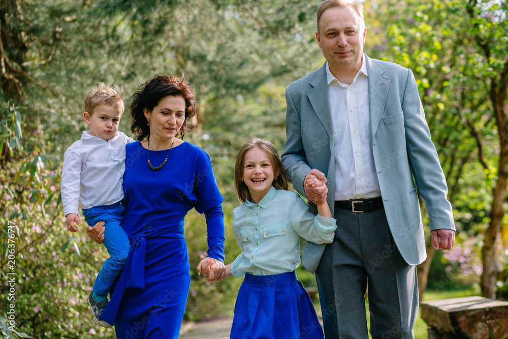 Lovely young family of four walking hand in hand in summer park. Lovely young family of four walking hand in hand in summer park.