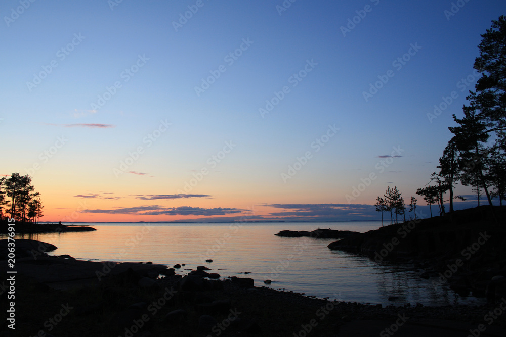 Obraz premium Beautiful northern landscape. Russian North. Ladoga lake at sunset. Wild nature. Trees reflected in the water. Aged photo in retro style. Summertime. Twilight. Island of Valaam, Karelia, Russia.