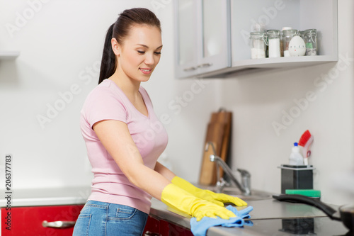 household  cleaning and people concept - happy woman or housewife in rubber gloves wiping table with microfiber cloth at home kitchen