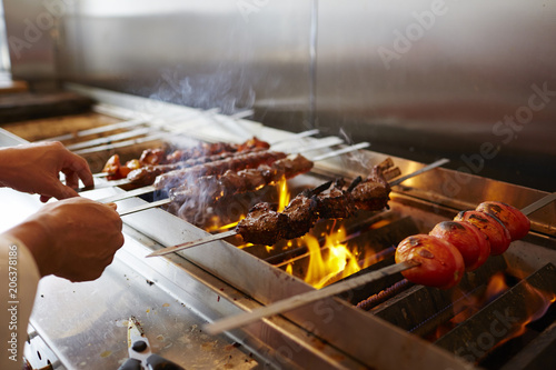 Cropped hands of chef making kebab on barbecue grill in commercial kitchen photo