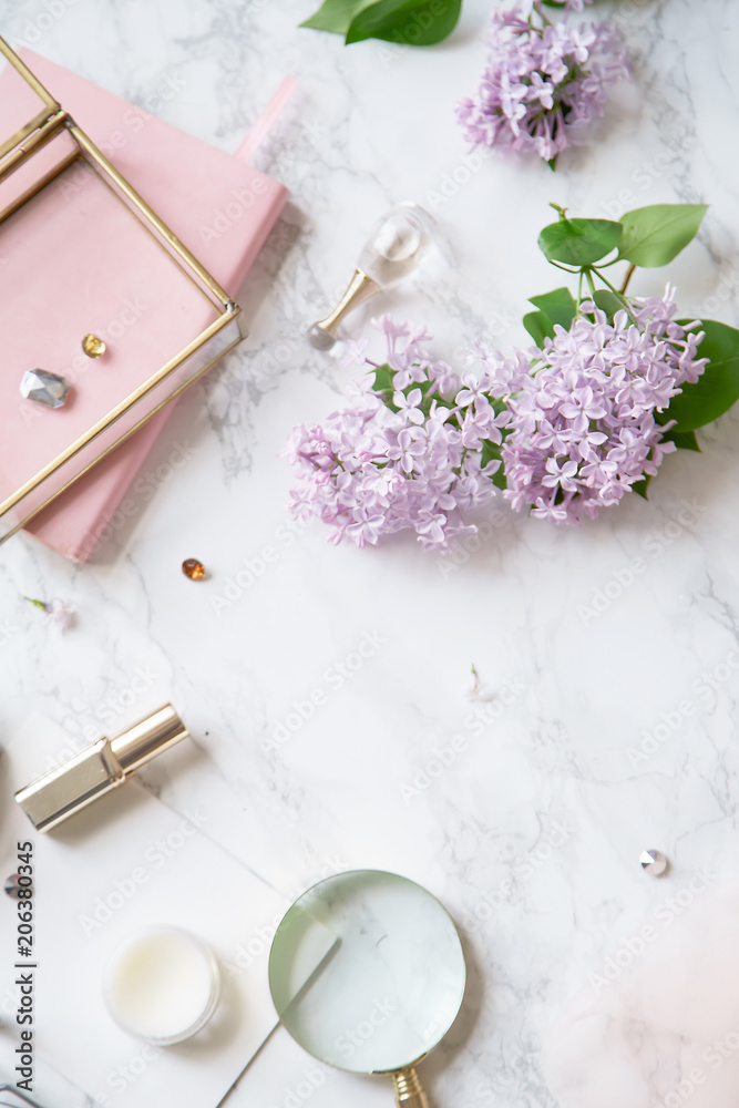 Top vew composition with feminine workspace mock up with lilac flowers and pink accessories on marble background Top vew composition with feminine workspace mock up with lilac flowers and pink accessories on marble background