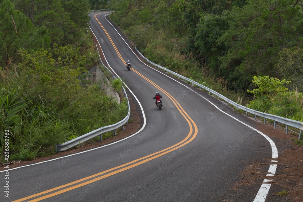 Beautiful mountain asphalt road with curve and double yellow line with two bikers riding motorbike, moto trip in north thailand Beautiful mountain asphalt road with curve and double yellow line with two bikers riding motorbike, moto trip in north thailand