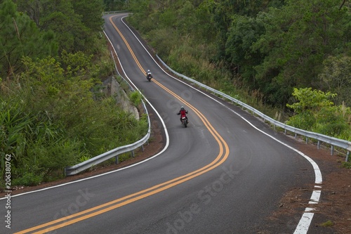 Beautiful mountain asphalt road with curve and double yellow line with two bikers riding motorbike, moto trip in north thailand