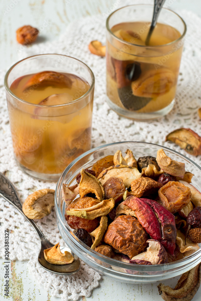 
  A mixture of dried fruits in a small round glass bowl, next to two glasses with compote on an old table. Delicious and healthy drink.